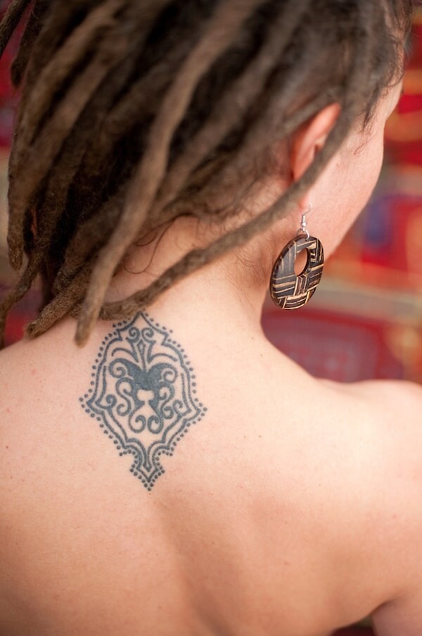 Close up of the back of a dreadlocked woman's bare neck with focus on her generic paisly tattoo.